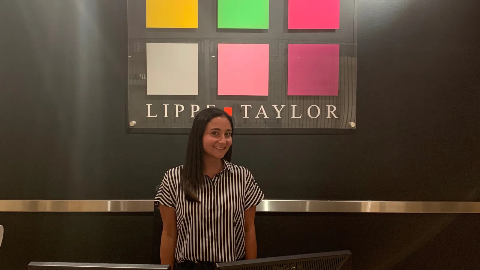 Naomi Posner posing in front of the Lippe Taylor logo